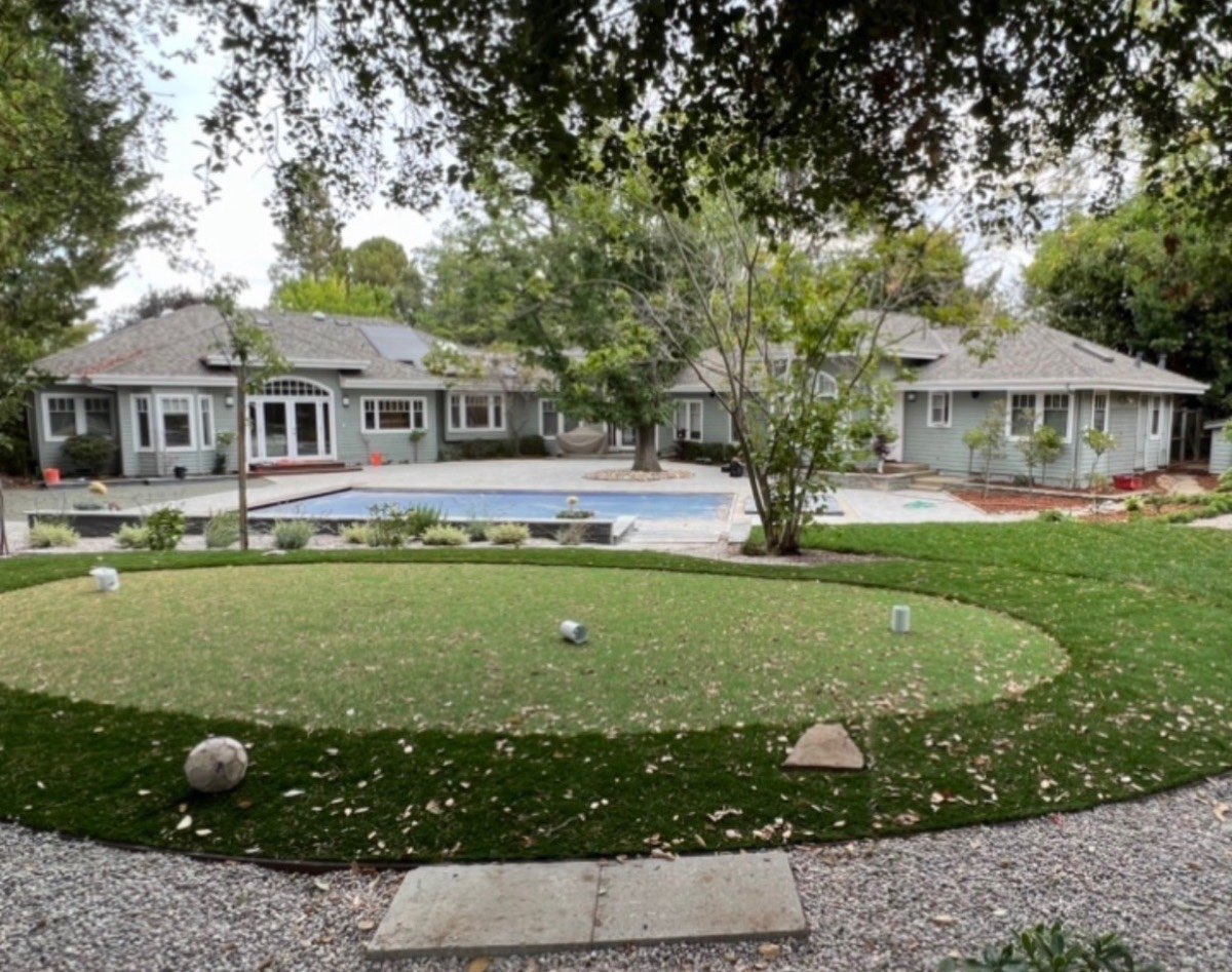 Spacious backyard with curved lawn, rectangular swimming pool, raised planter beds and mature trees