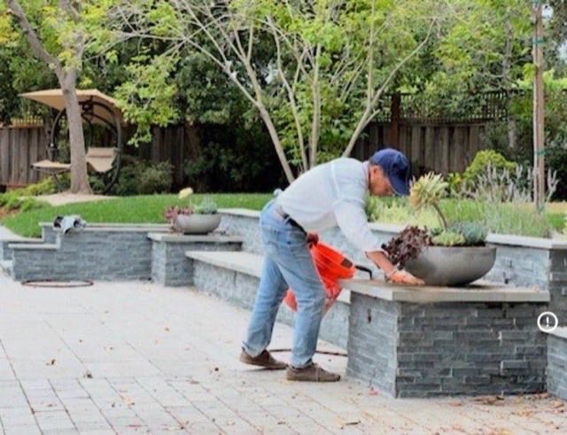 Landscaper planting succulents in concrete bowl planter on stacked stone retaining wall with patio and seating