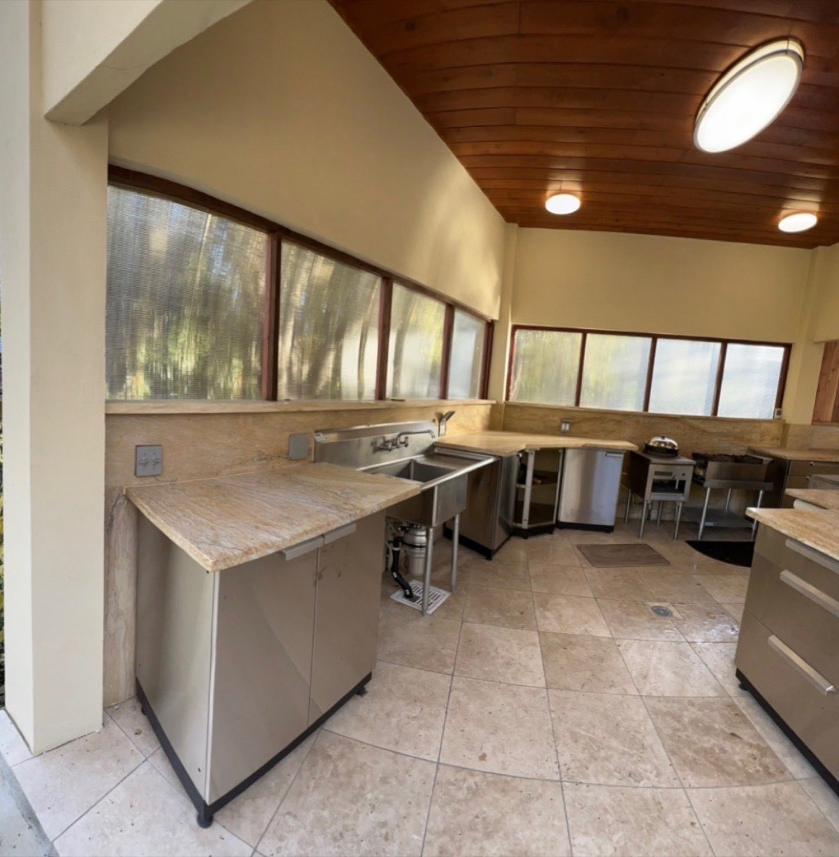 Covered outdoor kitchen with natural stone countertops, stainless steel appliances and warm wood ceiling