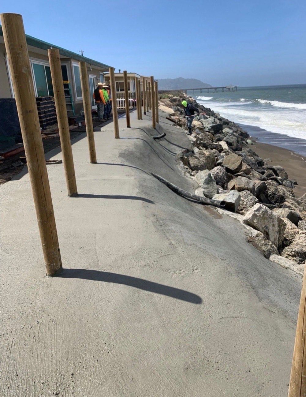 Coastal erosion control project with wood foundation posts, concrete walkway and boulder riprap along oceanfront
