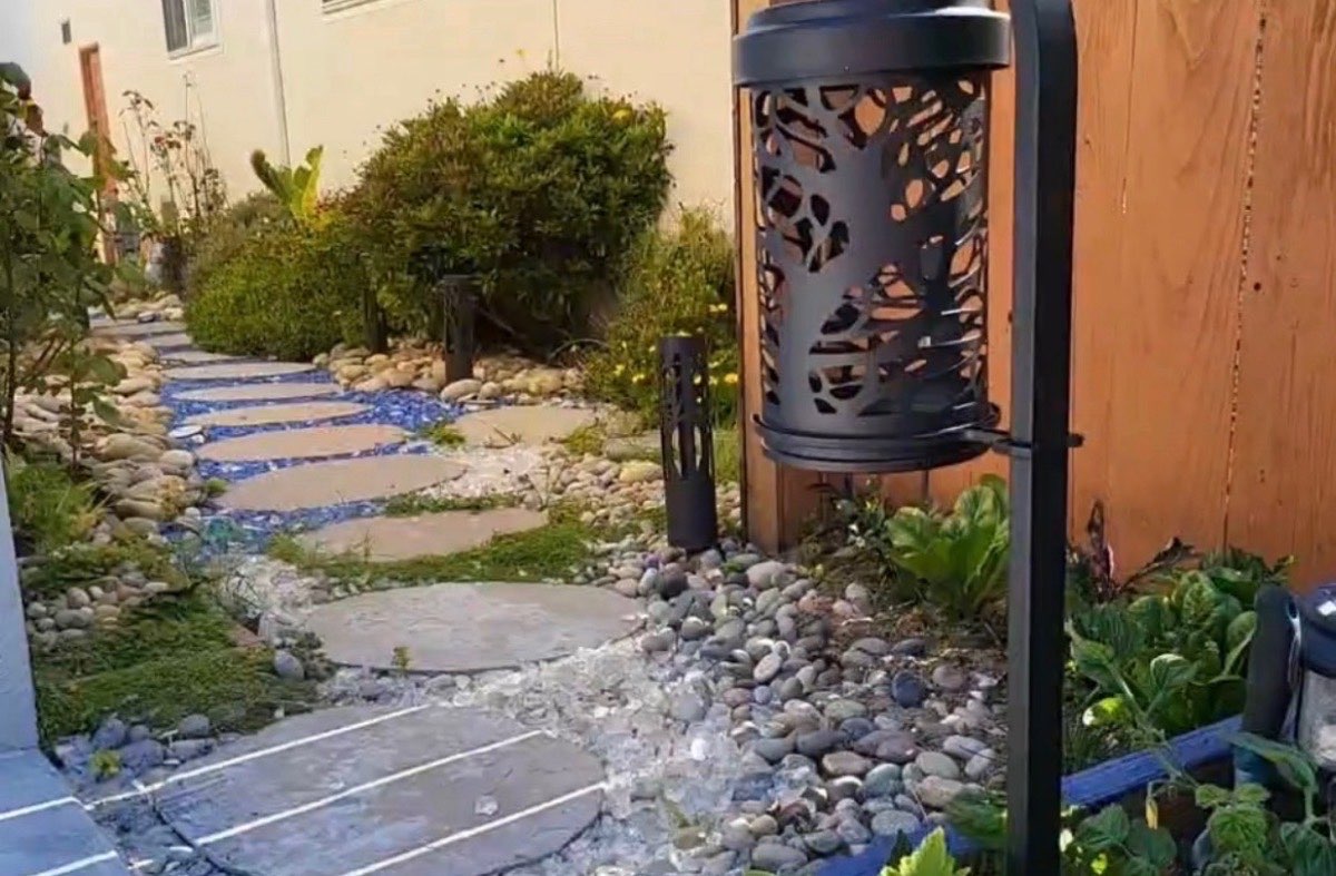 Garden pathway with natural flagstone stepping stones among river rock and decorative garden lantern with path lights